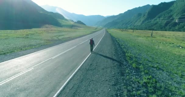 Vol au-dessus de l'auto-stoppeur touristique marchant sur la route asphaltée. Grande vallée rurale au jour d'été. Sac à dos randonneur gars. — Video