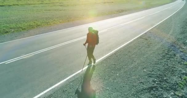 Repülés egy stoppos turista felett, aki aszfalt úton sétál. Hatalmas vidéki völgy a nyári napokon. Hátizsákos túrázó.. — Stock videók