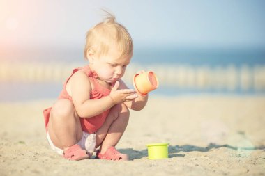 Denize yakın kumlu plajda oynayan Kırmızı elbiseli kız bebek. 