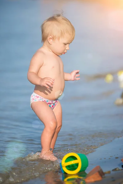 Lindo bebé jugando en la playa de arena y en agua de mar . — Foto de Stock