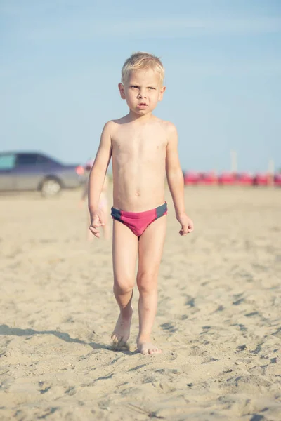 Menino bonito andando na praia de areia perto do mar. Costa oceânica . — Fotografia de Stock