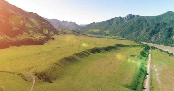 Aerial rural mountain road and meadow at sunny summer morning. Asphalt highway and river. — Stock Video