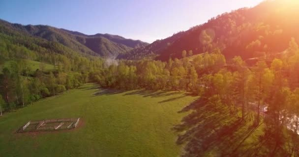 Mid air flight over fresh mountain river and meadow at sunny summer morning. Rural dirt road below. — Stock Video