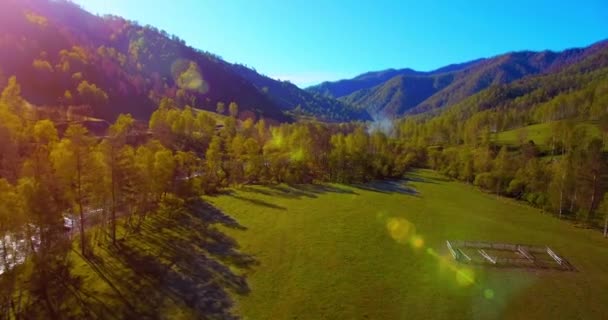 Mid air flight over fresh mountain river and meadow at sunny summer morning. Rural dirt road below. — Stock Video