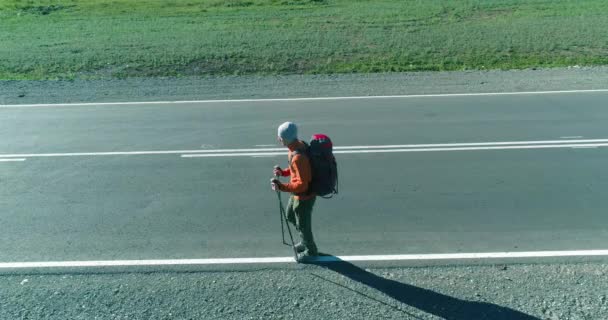 Volo sopra autostoppista turistico a piedi su strada asfaltata. Enorme valle rurale durante la giornata estiva. Zaino escursionista ragazzo. — Video Stock