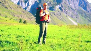 Sırt çantası ile yeşil dağ çayır üzerinde yürüyen adam hiking. Yaz spor ve eğlence kavramı.