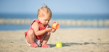Denize yakın kumlu plajda oynayan Kırmızı elbiseli kız bebek. 