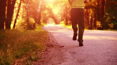 Asfalt yolda koşan sporcu. Kırsal şehir parkı. Yeşil ağaç ormanı ve ufukta güneş ışığı.