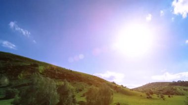 Yazın 4K UHD dağ çayırı zaman dilimi. Bulutlar, ağaçlar, yeşil çimenler ve güneş ışınları hareketi.