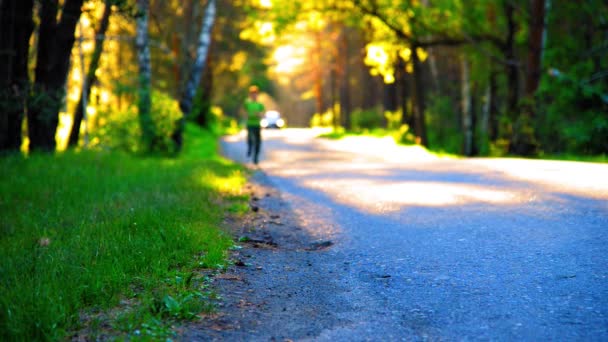 Homem do desporto a correr na estrada de asfalto. Parque rural da cidade. Floresta de árvore verde e raios de sol no horizonte. — Vídeo de Stock