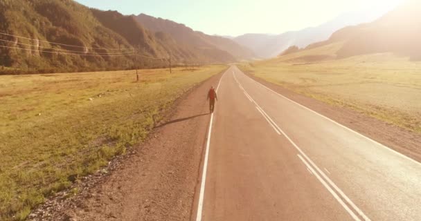 Vuelo sobre autoestopista turista caminando por carretera asfaltada. Gran valle rural en el día de verano. Mochila senderismo chico. — Vídeos de Stock