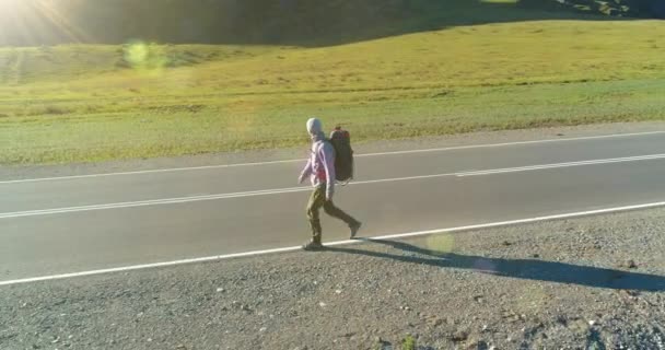 Voo sobre carona turista andando na estrada de asfalto. Vale rural enorme no dia de verão. Mochila caminhadas cara. — Vídeo de Stock