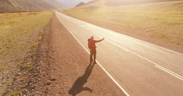 アスファルトの道路を歩くヒッチハイカーの観光客の上のフライト。夏の日に巨大な田舎の谷。リュックハイキング男. — ストック動画