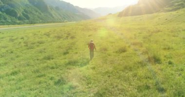 Sırt çantasıyla gezen turist yeşil dağ tarlasında yürüyor. Yaz günü büyük kırsal vadi.