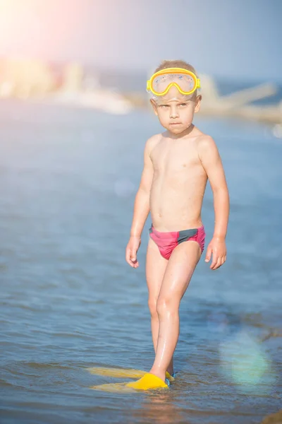 Cute little kid wearing mask and flippers for diving at sand tropical beach.