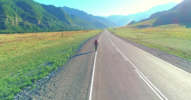 Volo sopra autostoppista turistico a piedi su strada asfaltata. Enorme valle rurale durante la giornata estiva. Zaino escursionista ragazzo. — Video Stock