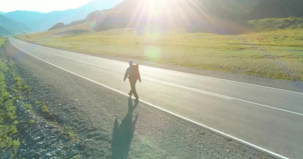 Vuelo sobre autoestopista turista caminando por carretera asfaltada. Gran valle rural en el día de verano. Mochila senderismo chico. — Vídeos de Stock