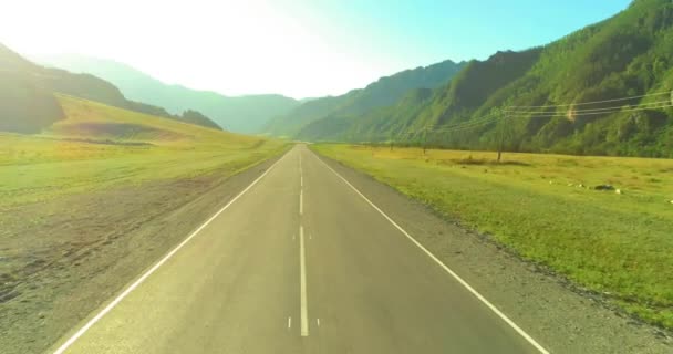 Voo aéreo de baixo ar sobre a estrada da montanha e o prado na ensolarada manhã de verão . — Vídeo de Stock