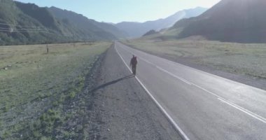 Asfalt yolda yürüyen otostopçu turist üzerinden uçuş. Yaz günü büyük bir kırsal vadi. Sırt çantalı gezgin..