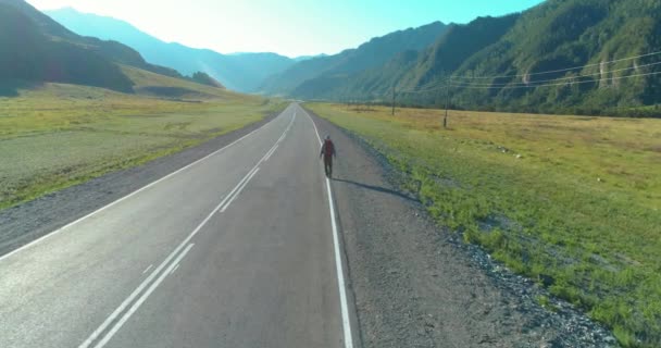 Volo sopra autostoppista turistico a piedi su strada asfaltata. Enorme valle rurale durante la giornata estiva. Zaino escursionista ragazzo. — Video Stock