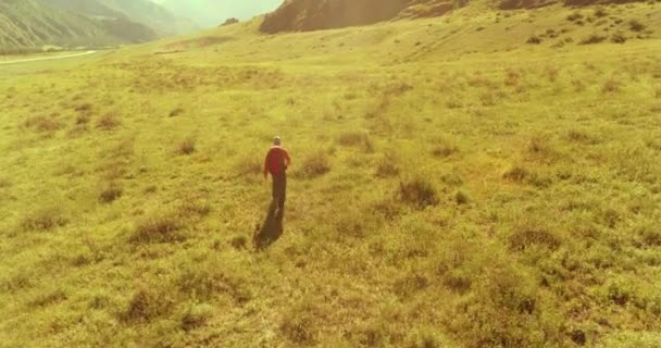 Vuelo sobre mochila senderismo turista caminando a través de campo de montaña verde. Gran valle rural en el día de verano. — Vídeos de Stock