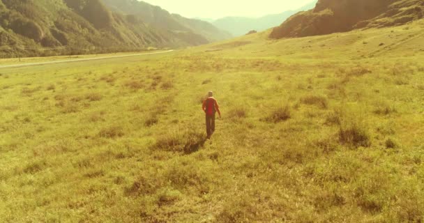 Політ над рюкзаком пішохідний турист, що йде через зелене гірське поле. Величезна сільська долина в літній день . — стокове відео