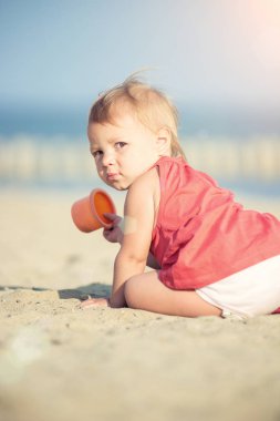 Denize yakın kumlu plajda oynayan Kırmızı elbiseli kız bebek. 