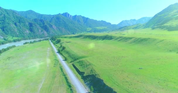 Aerial rural mountain road and meadow at sunny summer morning. Asphalt highway and river. — Stock Video