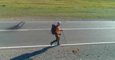 Asfalt yolda yürüyen otostopçu turist üzerinden uçuş. Yaz günü büyük bir kırsal vadi. Sırt çantalı gezgin..
