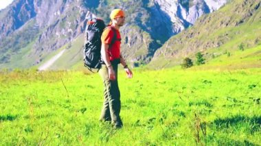 Sırt çantası ile yeşil dağ çayır üzerinde yürüyen adam hiking. Yaz spor ve eğlence kavramı.