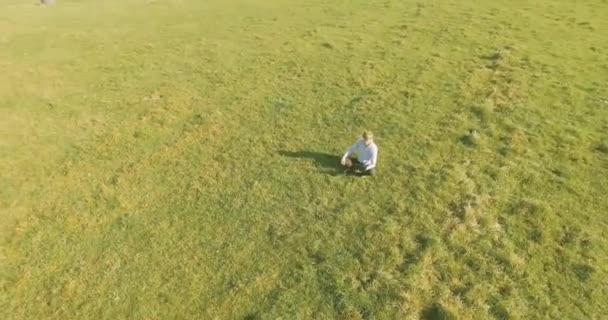 UHD 4k вид с воздуха. Низкий орбитальный полет над бизнесменом, сидящим на зеленой траве с блокнотом на поле — стоковое видео