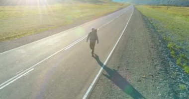 Asfalt yolda yürüyen otostopçu turist üzerinden uçuş. Yaz günü büyük bir kırsal vadi. Sırt çantalı gezgin..