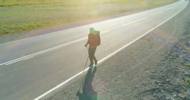 Hava 4K UHD görüntüsü. Asfalt yolda yürüyen otostopçu turist üzerinde alçak irtifa uçuşu. Büyük bir kırsal vadi ve yaz günü güneşli bir çayır. Sırt çantalı gezgin..