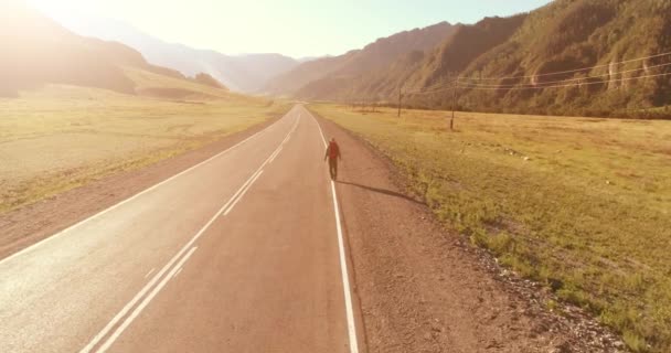 Vuelo sobre autoestopista turista caminando por carretera asfaltada. Gran valle rural en el día de verano. Mochila senderismo chico. — Vídeo de stock