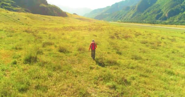 緑の山のフィールドを横断するバックパックハイキング観光客の上のフライト。夏の日の巨大な田舎の谷. — ストック動画