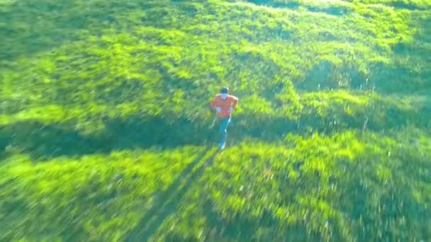 Vuelo sobre el hombre deportivo corriendo en la hierba verde perfecta pradera rural offroad. Puesta de sol en montaña — Vídeo de stock