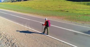 Asfalt yolda yürüyen otostopçu turist üzerinden uçuş. Yaz günü büyük bir kırsal vadi. Sırt çantalı gezgin..