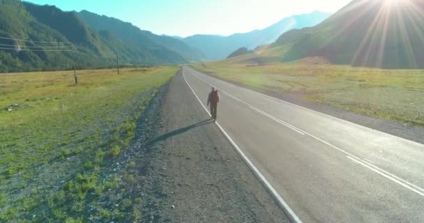 アスファルトの道路を歩くヒッチハイカーの観光客の上のフライト。夏の日に巨大な田舎の谷。リュックハイキング男. — ストック動画