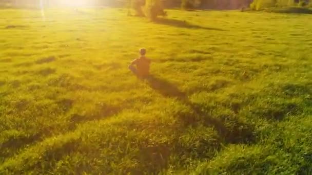 Vuelo radial de baja altitud sobre el hombre del yoga del deporte en hierba verde perfecta. Puesta de sol en montaña. — Vídeo de stock