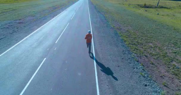 Uhd 4K航空ビュー 完璧なアスファルトの道路でスポーツマンの前で低高度飛行 山の日の出 地平線に緑の牧草地や太陽の光線 高速水平移動 — ストック動画