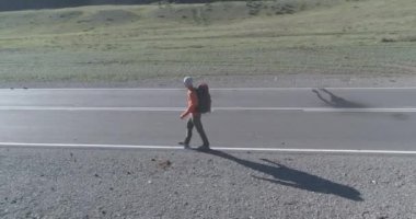 Asfalt yolda yürüyen otostopçu turist üzerinden uçuş. Yaz günü büyük bir kırsal vadi. Sırt çantalı gezgin..