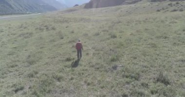 Sırt çantasıyla gezen turist yeşil dağ tarlasında yürüyor. Yaz günü büyük kırsal vadi.