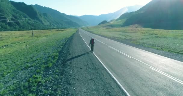 Asfalt yolda yürüyen otostopçu turist üzerinden uçuş. Yaz günü büyük bir kırsal vadi. Sırt çantalı gezgin.. — Stok video