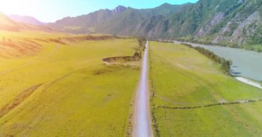 Güneşli yaz sabahında havadan kırsal dağ yolu ve çayır. Asfalt karayolu ve nehir.