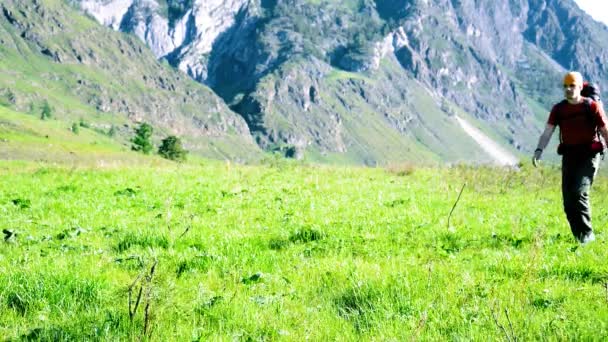 Sırt çantası ile yeşil dağ çayır üzerinde yürüyen adam hiking. Yaz spor ve eğlence kavramı. — Stok video