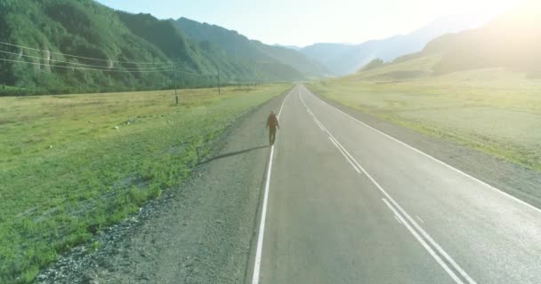 Vlucht over lifter toerist wandelen op asfalt weg. Enorme landelijke vallei op zomerdag. Rugzakwandelaar. — Stockvideo