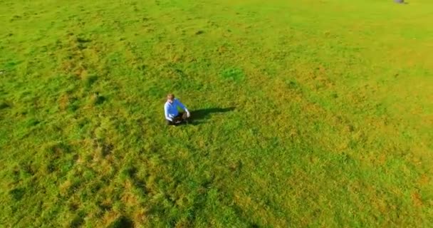 UHD 4k вид с воздуха. Низкий орбитальный полет над бизнесменом, сидящим на зеленой траве с блокнотом на поле — стоковое видео