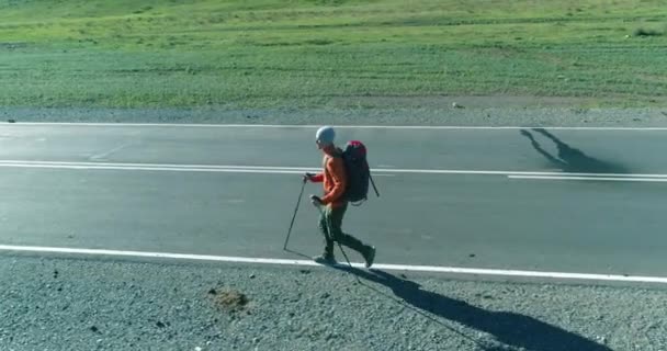 Vlucht over lifter toerist wandelen op asfalt weg. Enorme landelijke vallei op zomerdag. Rugzakwandelaar. — Stockvideo