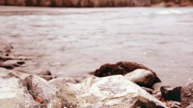 Dolly ormanın yakınındaki bir dağ nehrinde akan suyun kaygan görüntüsü. Islak kayalar ve güneş ışınları. Yatay sabit hareket.