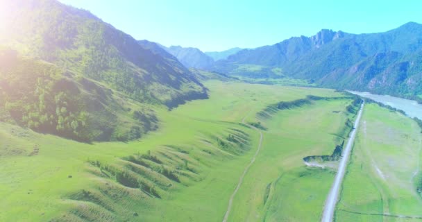 Luftlinie ländliche Bergstraße und Wiese an einem sonnigen Sommermorgen. Asphaltstraße und Fluss. — Stockvideo